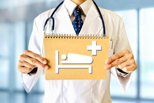 ベッドに＋と書かれた画用紙を持つ医者