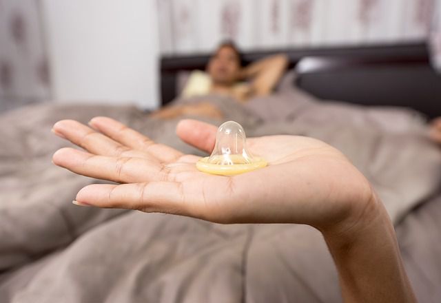 男性が寝ていベッドの前で手の上に乗せたコンドームを持つ手