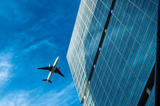 青空の中でビルの横を飛ぶ飛行機