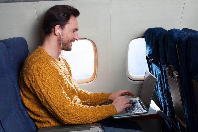 ニコニコしながら飛行機内でパソコンを操作する男性