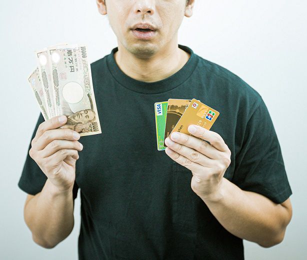 3万円とクレジットカードを3枚手に持つ男性