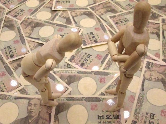 大量の1万円札の上で頭を下げる人形と偉そうに腕を組む人形