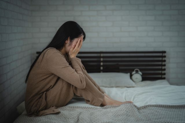 ベッドの上で顔を覆う女性