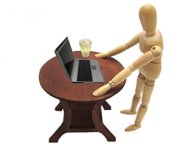 テーブルに載せられたノートパソコンを操作する木の人形