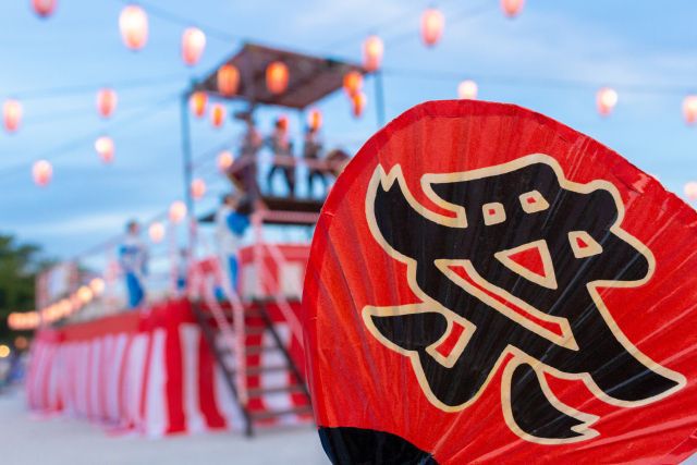 お祭りのやぐらの前にある祭と書かれたうちわ