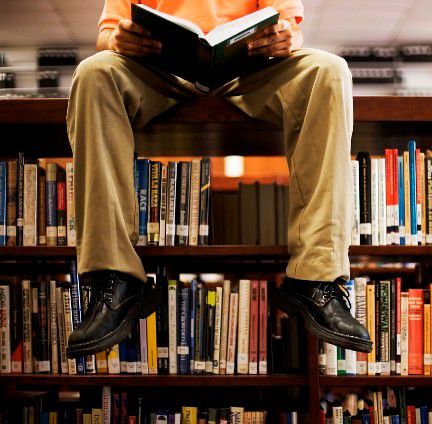 本棚の上に座って本を読む男性