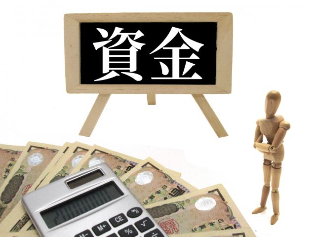 資金の看板の横で電卓と現金を見る木の人形