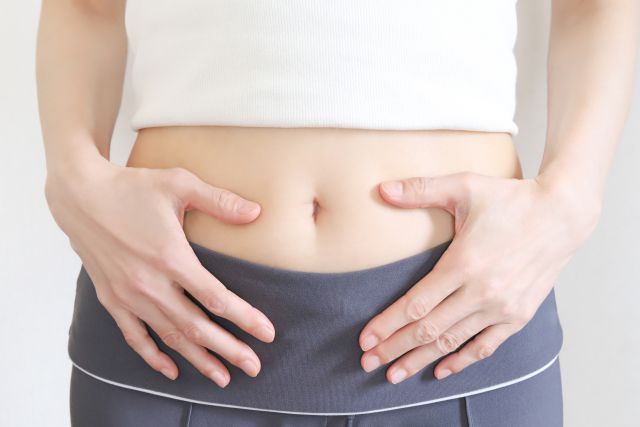 へそ出しのお腹を抑える女性