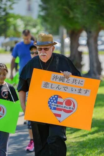「沖縄と共に悲しんでいます」というプレートを持つアメリカ人男性