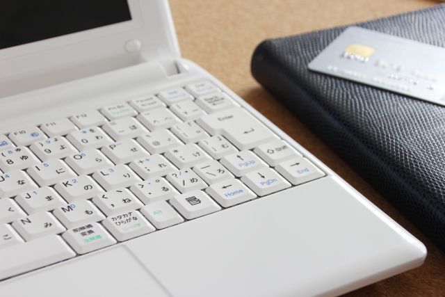 白いノートパソコンの横に置かれた財布とクレジットカード