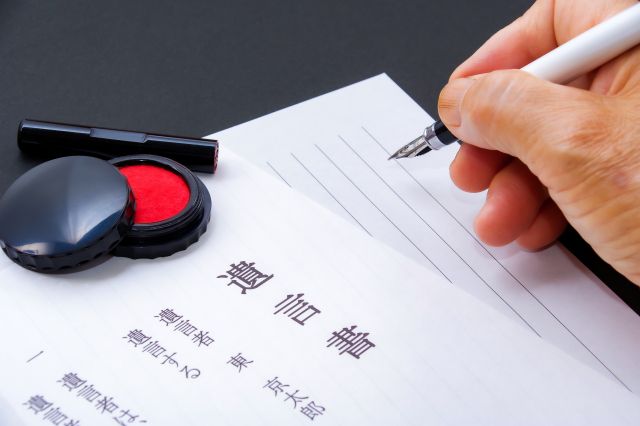 机に置かれた遺言状と紙に文字を書こうとしている人