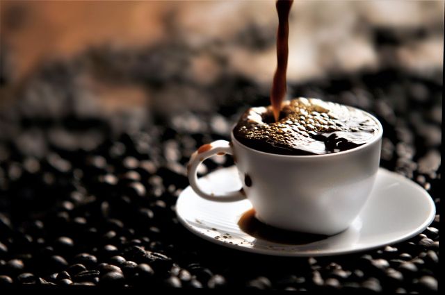 コーヒー豆の上のカップになみなみと注がれるコーヒー