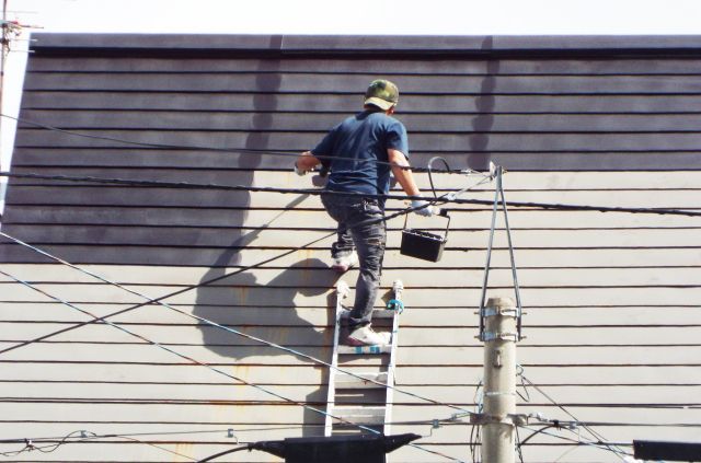 屋根の上に乗り塗装をする男性
