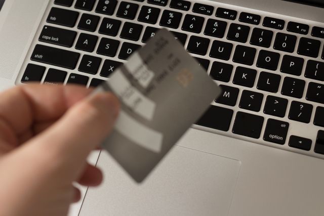 パソコンのキーボードの上でクレジットカードを持つ手