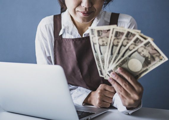 パソコンの前でお金を見せびらかす女性