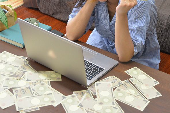 机の上のパソコンとお金を見る女