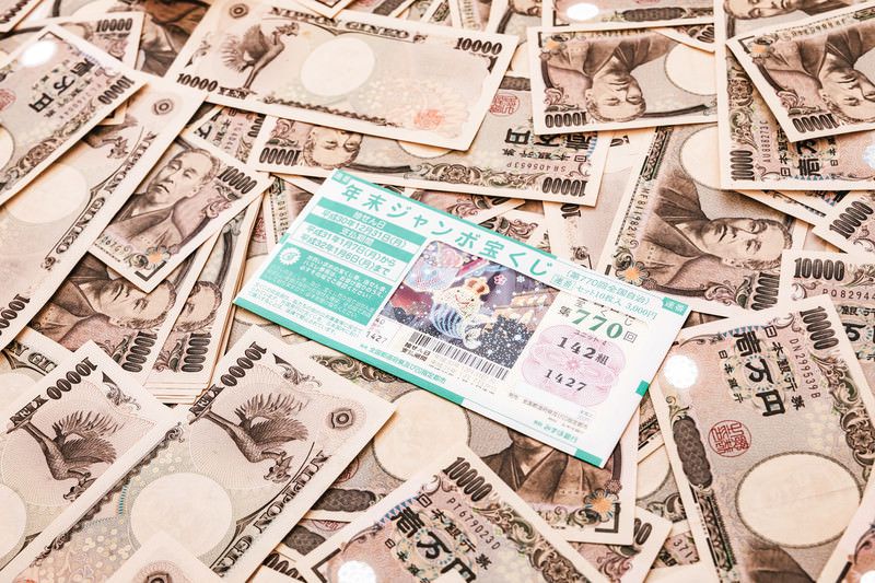 散乱する1万円札の真ん中に置かれた年末ジャンボ宝くじ